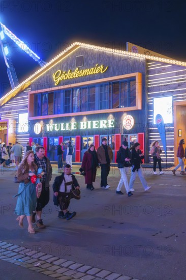 People strolling at night in front of an illuminated building at the funfair, Cannstatter Wasen
