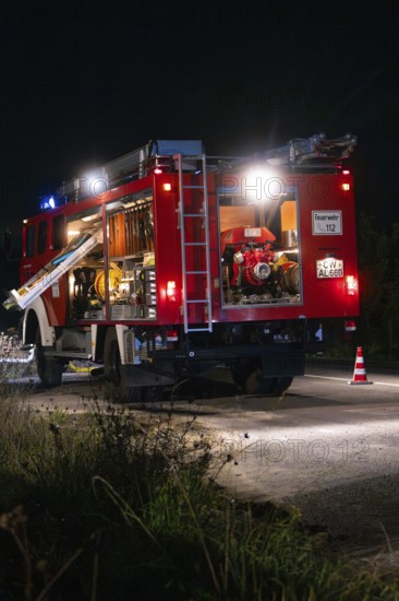 Fire engine at night with open back, illuminated by lanterns and blue lights, fire brigade exercise