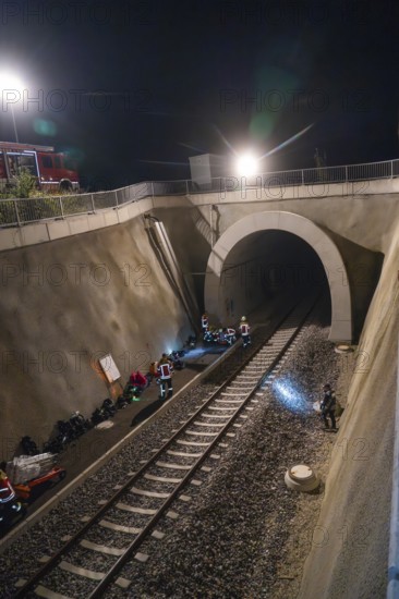 Rescue workers working in an illuminated tunnel at night, railway tracks in the foreground, fire