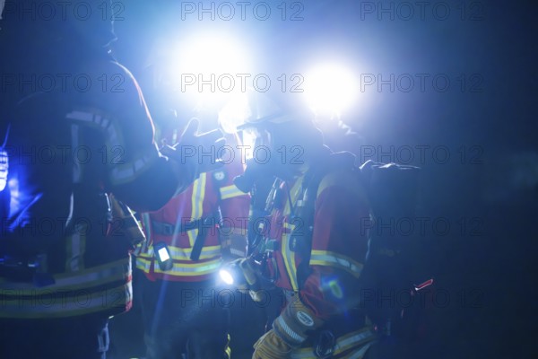 Firefighters illuminated with glare lights, in protective suits, on duty at night, firefighting