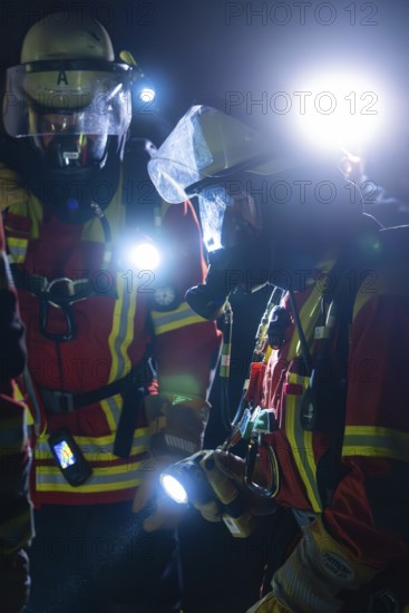 Two firefighters in protective clothing and breathing masks with torches in action at night, fire