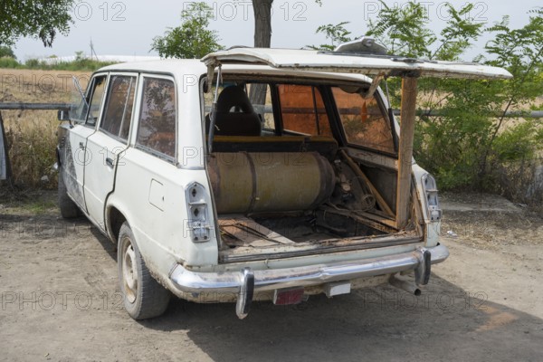 An old estate car with an open tailgate shows a gas bottle lying inside, car has gas tank