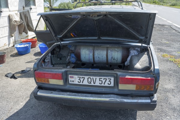 Old car with open boot, gas bottle and tools on a sunny day next to the road, car has gas tank
