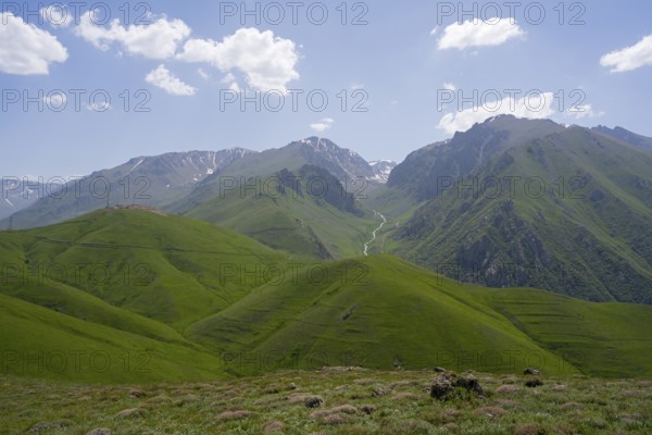 Green hills in front of mountains with clouds in the blue sky, at the highest pass of Armenia,