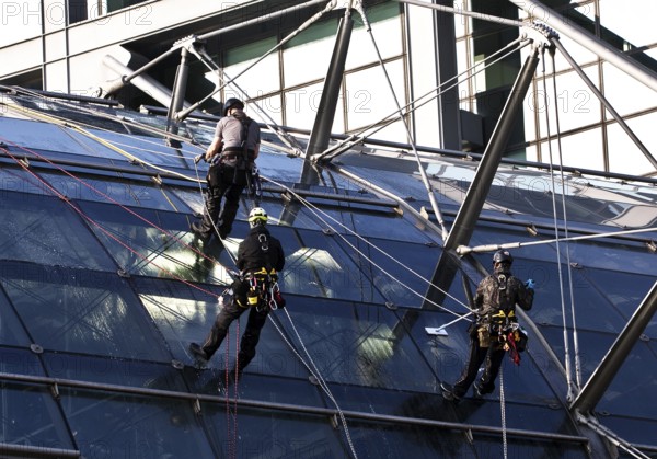 Three male glass cleaners abseiling down a glass roof of Berlin Central Station to clean windows,
