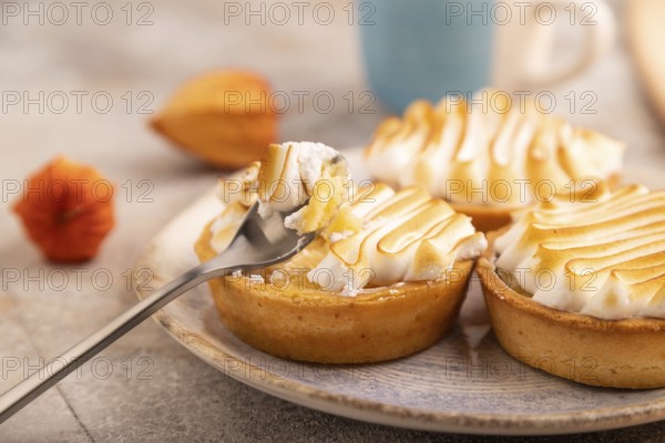 French lemon tart with meringue on brown concrete background, cup of coffee, orange linen textile,