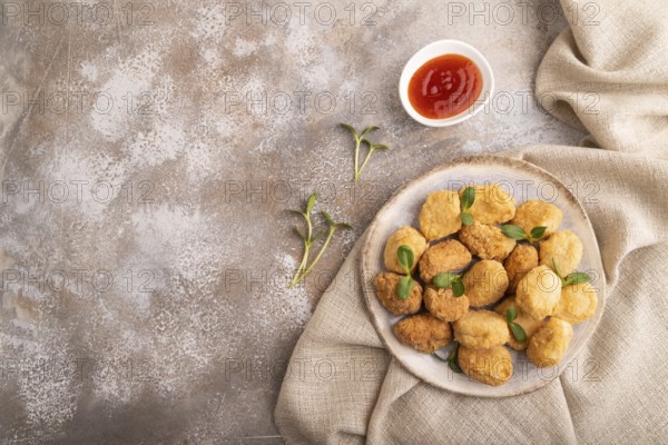 Fried crispy Chicken Nuggets with ketchup, microgreen on brown concrete background and linen