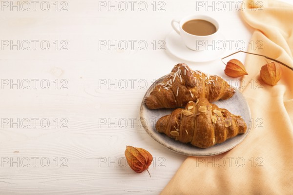 Croissant on blue plate on white wooden background and orange linen textile, cup of coffee, side