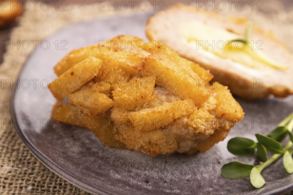 Chicken Schnitzel on gray plate with microgreen on brown wooden background and linen textile. side
