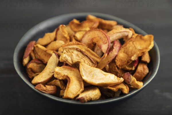 Dried Apples in ceramic bowl on black wooden background. Side view, close up. healthy food,