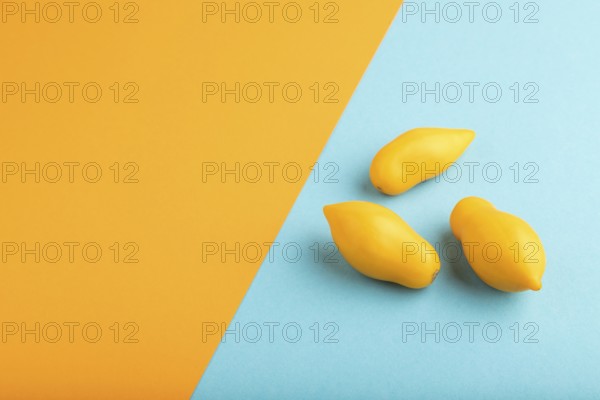 Yellow tomatoes on blue and orange pastel paper background. Side view, copy space. healthy food,
