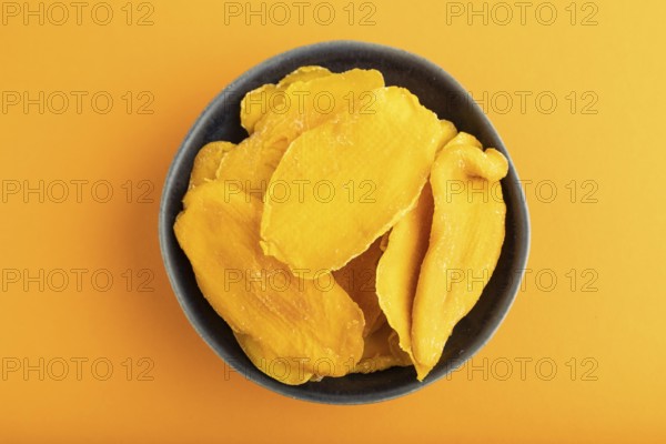 Dried Mango in blue ceramic bowl on orange pastel paper background. Top view, copy space, flat lay.