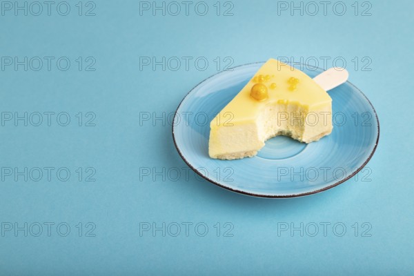 Bitten Yellow Cake pop with sprinkles on blue ceramic plate on blue pastel paper background, side