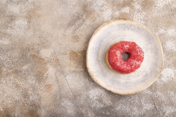 Pink Donut with sprinkles on blue ceramic plate on brown concrete background, top view, flat lay,