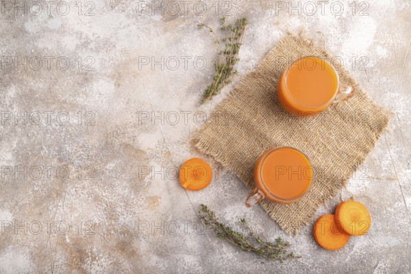 Two glasses with carrot juice, on brown concrete background and linen textile. Diet, healthy eating