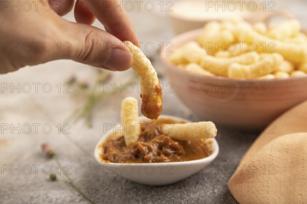 Corn flakes sticks with hand with caramel in ceramic bowl on gray concrete background and orange