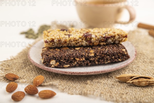 Granola bars with caramel, nuts, flakes in ceramic plate on white wooden background, beige linen