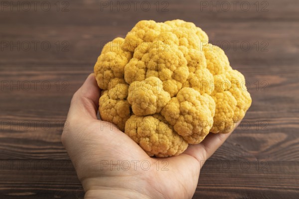 Yellow Cauliflower with hand on brown wooden background. Side view, close up. healthy food,
