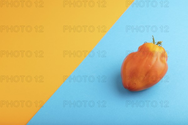 Red Heart Shape tomato on blue and orange pastel paper background. Side view, copy space. healthy