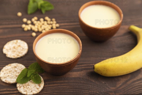 Organic non dairy banana and soy milk in clay cup on brown wooden background. Vegan healthy food
