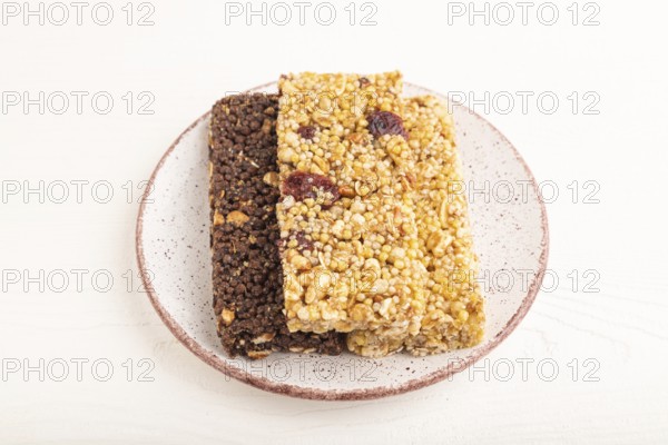 Granola bars with caramel, nuts, flakes in ceramic plate on white wooden background. Side view,
