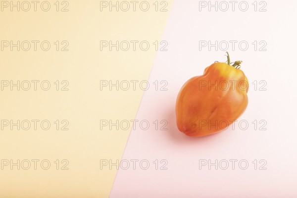Red Heart Shape tomato on pink and orange pastel paper background. Side view, copy space. healthy