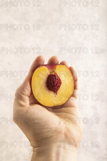 Peach Cut in half with hand on brown concrete background. Side view, copy space. healthy food,