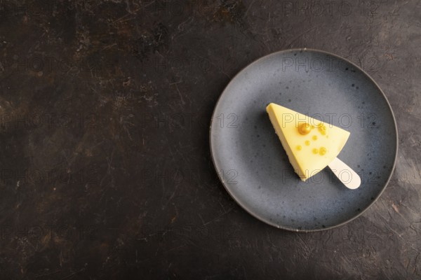Yellow Cake pop with sprinkles on blue ceramic plate on black concrete background, top view, flat