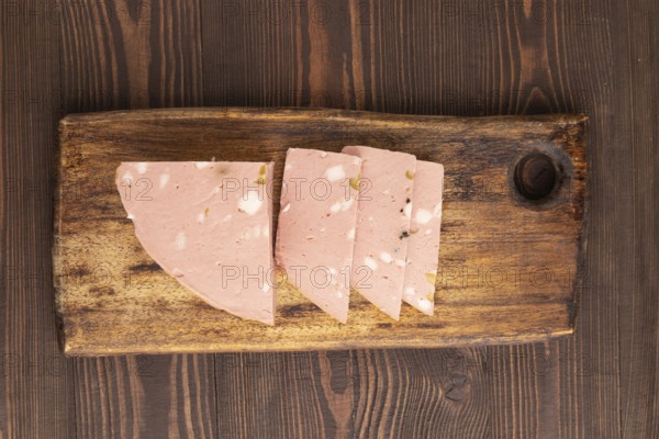Mortadella sausage on wooden cutting board with pepper and herbs on brown wooden background. Top
