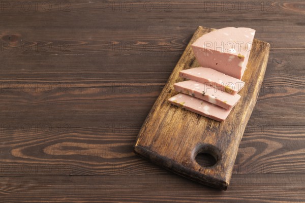 Mortadella sausage on wooden cutting board with pepper and herbs on brown wooden background. Side