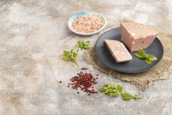 Mortadella sausage on plate with pepper and herbs on brown concrete background and linen textile.