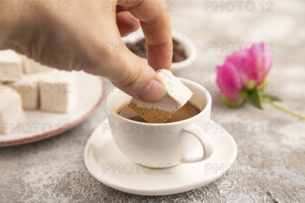 Coffee marshmallow with cup of coffee with hand on brown concrete background. side view, close up,