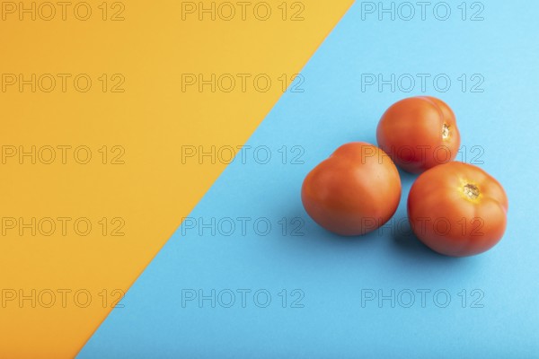 Red tomato on blue and orange pastel paper background. Side view, copy space. healthy food,