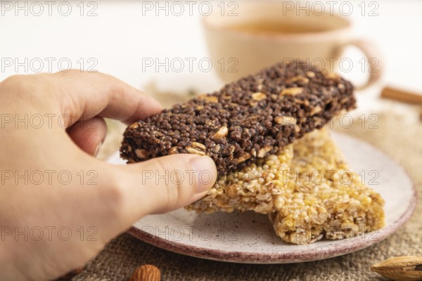 Granola bars with caramel, nuts, flakes in ceramic plate with hand on white wooden background,