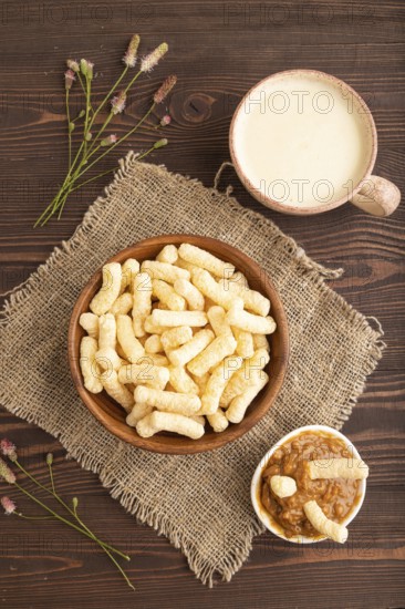 Corn flakes sticks with caramel in wooden bowl on brown wooden background and linen textile. Top
