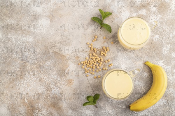 Organic non dairy banana and soy milk in glass on brown concrete background. Vegan healthy food
