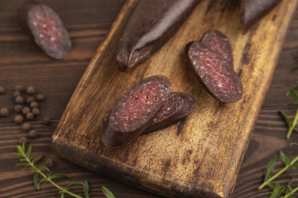 Sujuk sausage on wooden cutting board with pepper and herbs on brown wooden background. Side view,