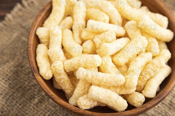 Corn flakes sticks with caramel in wooden bowl on brown wooden background and linen textile. Side
