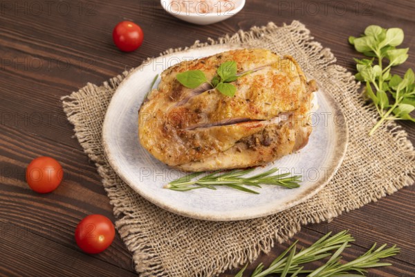 Fried Turkey Thigh with spices and rosemary on plate on brown wooden background and linen textile.