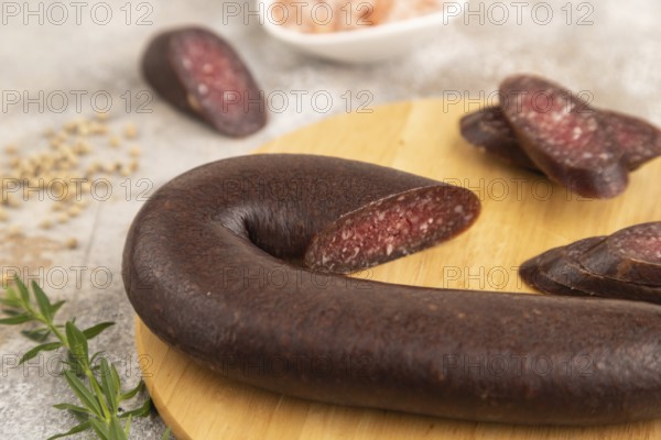 Sujuk sausage on wooden cutting board with pepper and herbs on brown concrete background. Side