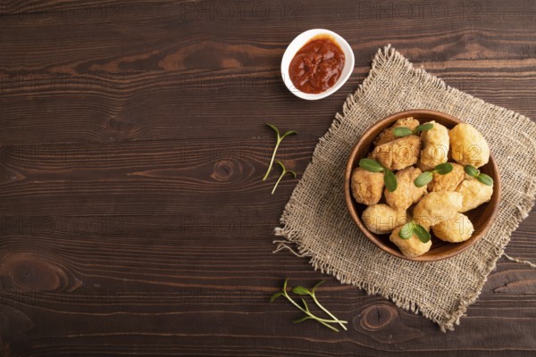 Fried crispy Chicken Nuggets with ketchup, microgreen on brown wooden background and linen textile.
