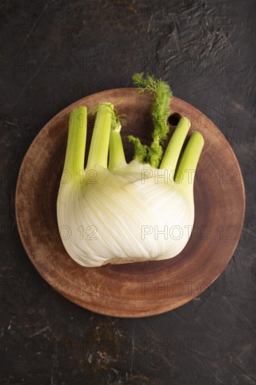 Fresh Fennel bulb on wooden cutting board on black concrete background, top view, flat lay, copy