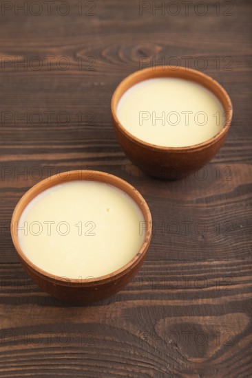 Organic non dairy banana and soy milk in clay cup on brown wooden background. Vegan healthy food