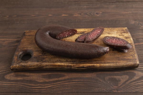 Sujuk sausage on wooden cutting board with pepper and herbs on brown wooden background. Side view,