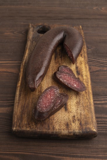 Sujuk sausage on wooden cutting board with pepper and herbs on brown wooden background. Side view,
