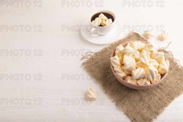 Orange and pink marshmallow in ceramic bowl on white wooden background and linen textile, side