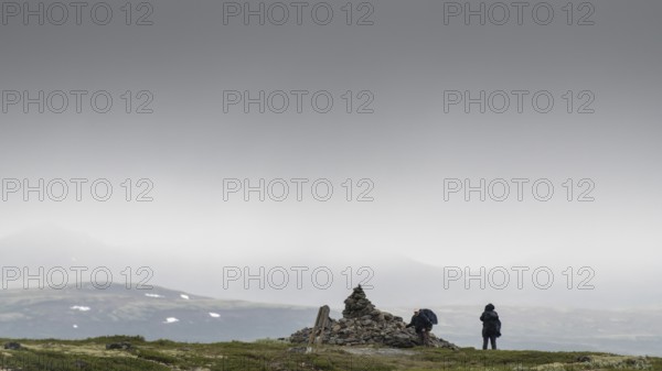 Two pilgrims lay stones at the stone pyramid Allmannrøysa, cloudy landscape, pilgrimage route