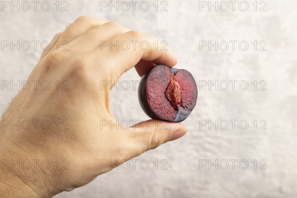 Purple Plum Cut in half with hand on gray concrete background. Side view, close up. healthy food,