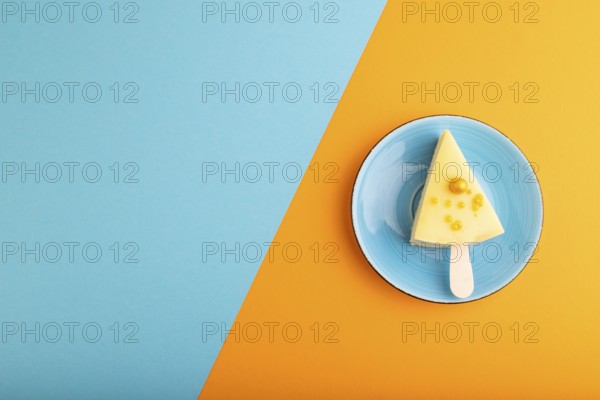 Yellow Cake pop with sprinkles on blue ceramic plate on blue and orange pastel paper background,