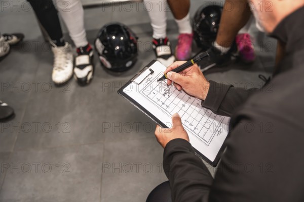 American football coach holding a clipboard, drawing strategies on a field diagram, instructing